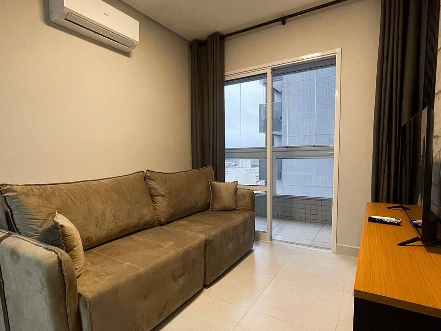 Ein modernes Wohnzimmer mit einer Couch, einem Fernsehschrank und einer Glastür, die auf einen Balkon führt.