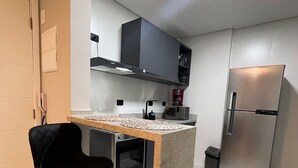 A compact kitchen with a central island, a built-in oven, a refrigerator, and black cabinets. - UNITA 157 (Praia Grande)