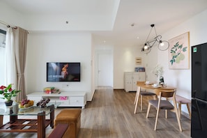 Een moderne woonkamer met een flatscreen televisie, een eethoek met een houten tafel en stoelen, een keuken en een gang die naar een andere kamer leidt.