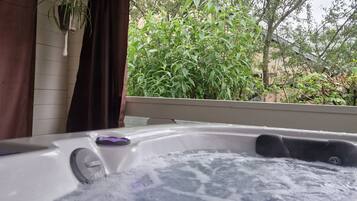 Relax in a hot tub surrounded by lush greenery and a serene view.