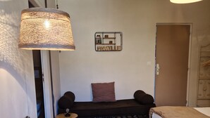 A cozy room with a wooden table, a green chair, a sofa with cushions, a bed, and a hanging lamp. - Une autre maison (Pupillin)