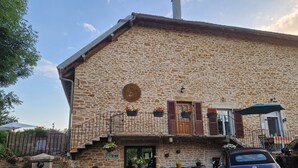A stone building with a wooden door, potted plants, and a car parked in front. - Une autre maison (Pupillin)