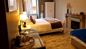 A bedroom with a bed, bedside table with a lamp, a small table with cups and a tray, a wardrobe, and a fireplace. - Une autre maison (Pupillin)