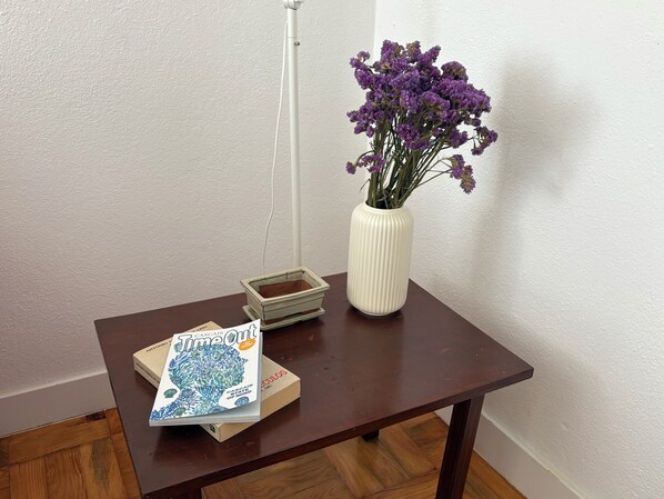 A wooden table with a white vase containing purple flowers, a stack of books, and a small box.