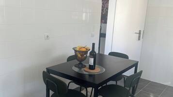 Uma área de refeições com uma mesa, quatro cadeiras, uma cesta de frutas e uma garrafa de vinho.