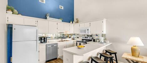 Cozinha moderna com armários brancos, uma parede de destaque azul, uma ilha central com banquetas e um lustre.