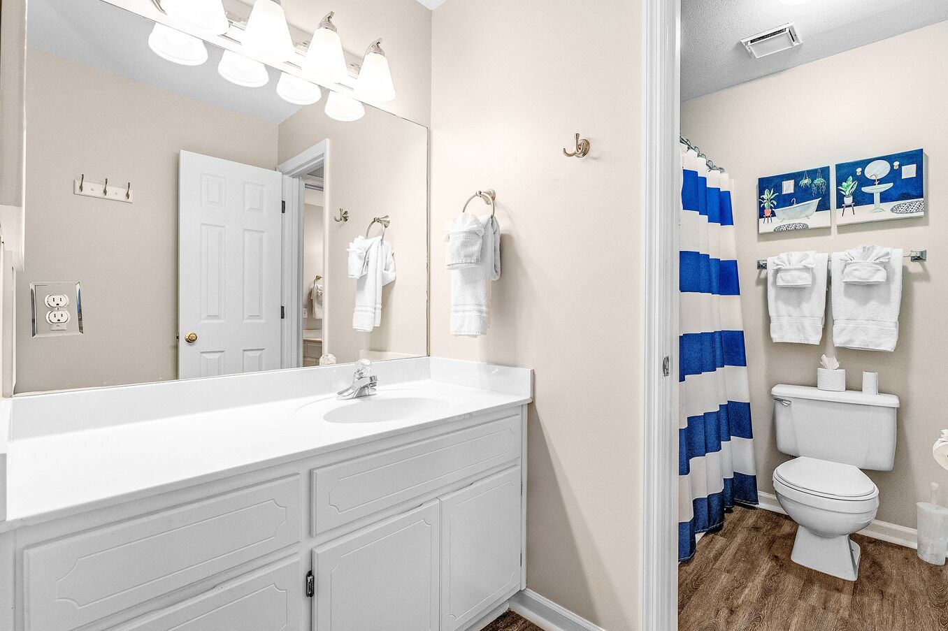 A bathroom with a white vanity, a large mirror, and a shower curtain with blue stripes.
