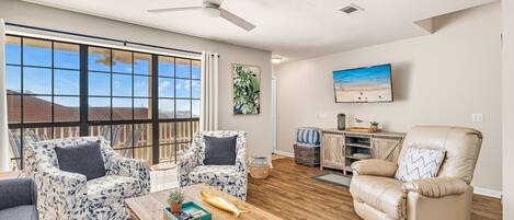A spacious living room with a large window, a ceiling fan, and a view of the outdoors.