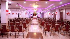 A spacious hall with rows of chairs arranged for an event, a stage at the front, and purple lighting. - Hotel River View (Khagaria)