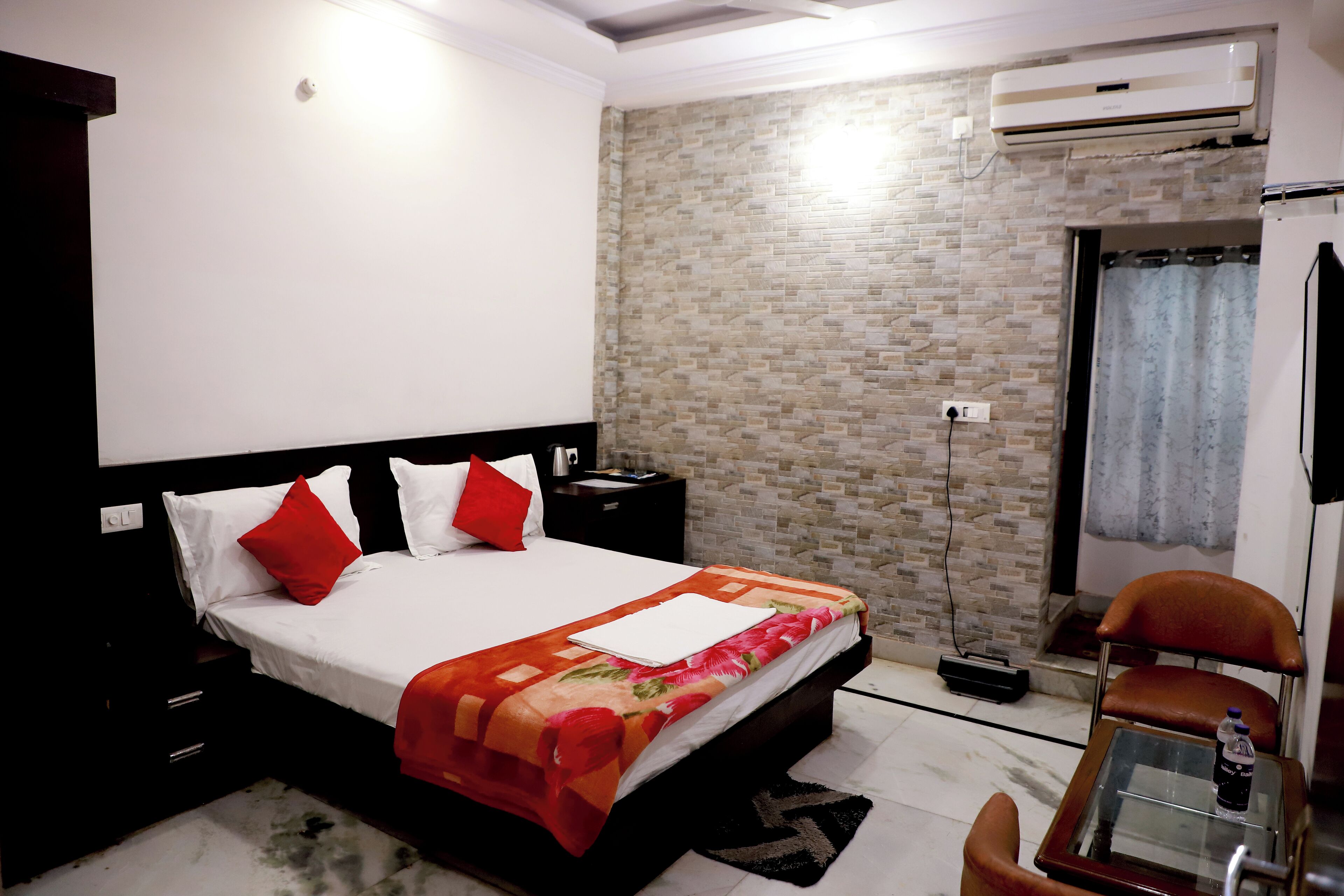 Una habitación de hotel con cama, mesita de noche, silla y equipo de aire acondicionado.