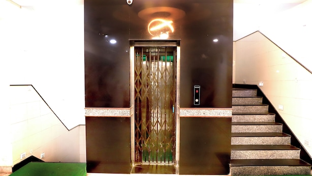 An elevator with a modern design, a staircase to the right, and a green carpet at the base. - Hotel River View (Khagaria)