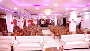 A spacious hall with rows of chairs and two white sofas, decorated with red and white balloons. - Hotel River View (Khagaria)