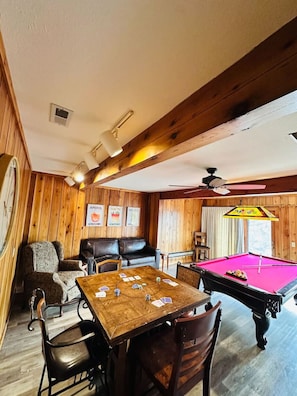 Une pièce chaleureuse avec des murs en bois, une table de billard, un canapé et une table à jouer aux cartes.