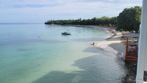Una playa con agua turquesa cristalina, un bote y una estructura de madera con sillas.