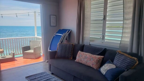 Un balcón con vista al océano, un sofá con cojines estampados y una silla de mimbre.