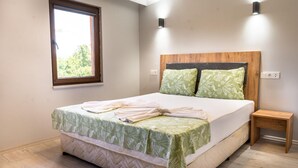 Un lit bien fait, recouvert d’une couvre-lit à motifs floraux verts, avec une tête de lit en bois et deux coussins verts. Une petite table de chevet en bois se trouve à côté du lit.