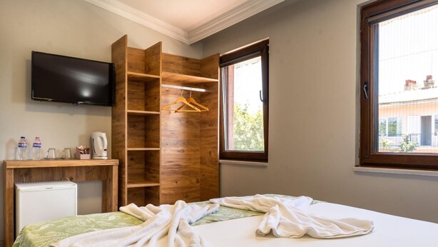 Une chambre à coucher avec un lit, une armoire en bois, un téléviseur et une fenêtre donnant sur des immeubles.