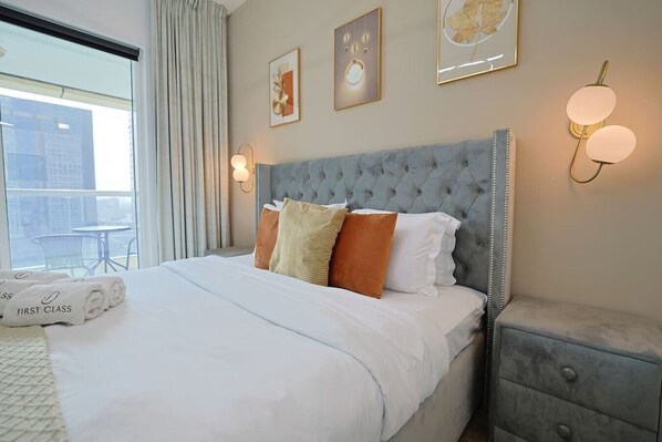 A hotel room with a large bed, a grey headboard, and a view of the city through the window.