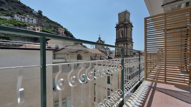 A balcony with a metal railing overlooking a building with a clock tower. - The Bell Tower Clock with terrace (Minori)
