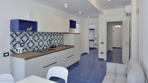 A modern kitchen with white cabinets, a wooden countertop, and a patterned backsplash. There is a sink, a kettle, and a chair in the dining area. - The Bell Tower Clock with terrace (Minori)