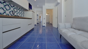 A hallway with a blue tiled floor, white walls, and a white sofa. - The Bell Tower Clock with terrace (Minori)