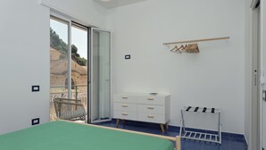 A bedroom with a bed, a dresser, a hanging rack, and a sliding glass door leading to a balcony. - The Bell Tower Clock with terrace (Minori)