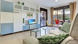 Ein modernes Wohnzimmer mit einer Couch, einem Glastisch, einem Fernseher und einem Essbereich mit Tisch und Stühlen.