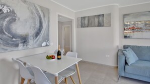 A modern living room with a white table set for two, a blue sofa, and abstract wall art. - Sun And Green, Heated Pool, 3 Rooms, Air C (San Miguel de Abona)