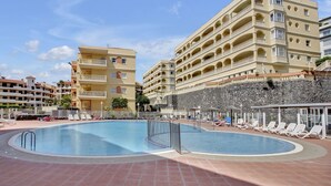 A swimming pool surrounded by lounge chairs and a multi-story hotel building with balconies. - Sun And Green, Heated Pool, 3 Rooms, Air C (San Miguel de Abona)