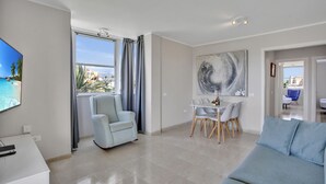 A modern living room with a sofa, a dining table with chairs, a TV mounted on the wall, and a large abstract painting. - Sun And Green, Heated Pool, 3 Rooms, Air C (San Miguel de Abona)