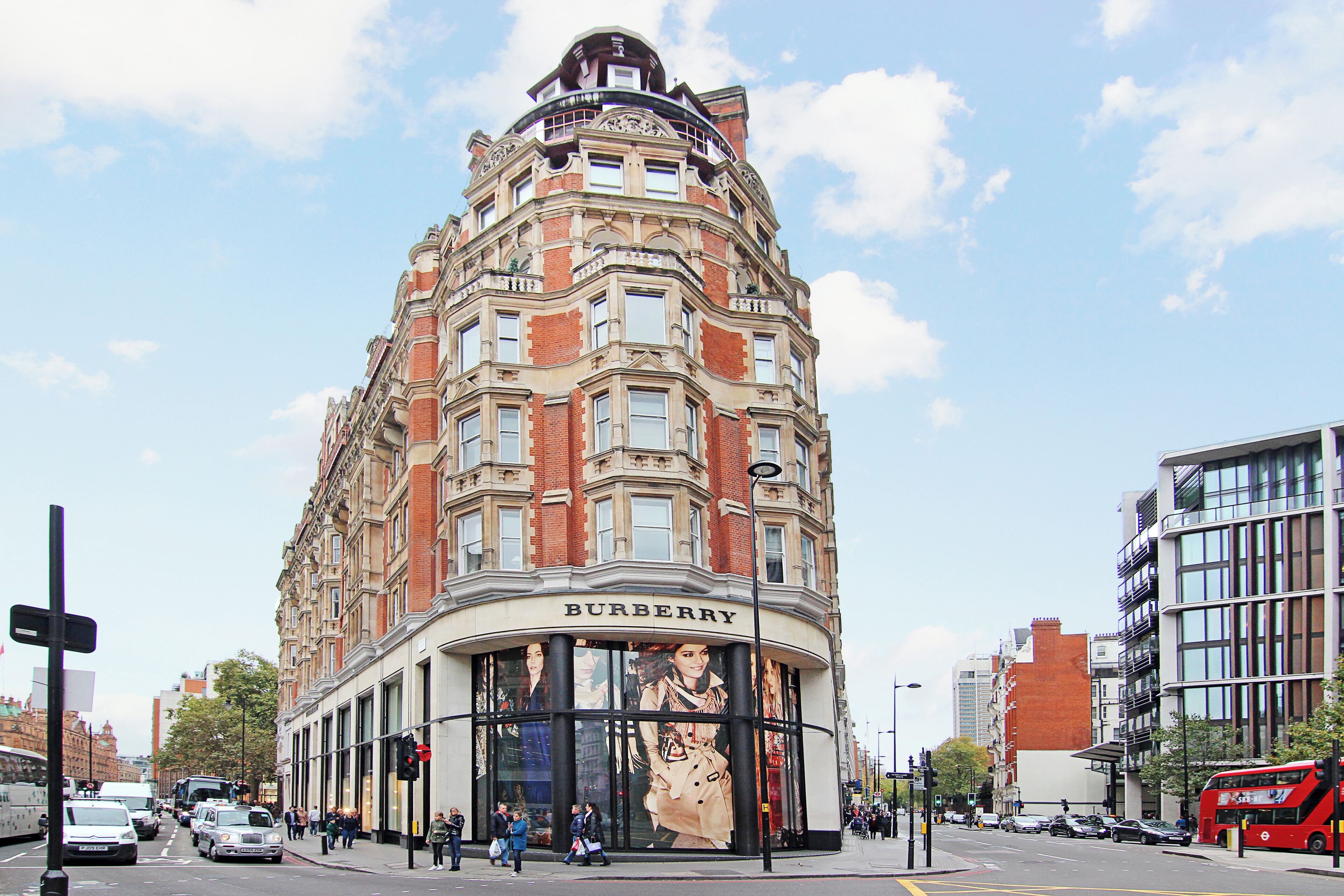 Un edificio ad angolo con un grande cartello Burberry, caratterizzato da uno stile architettonico classico con molte finestre e una sporgenza angolare ben definita.