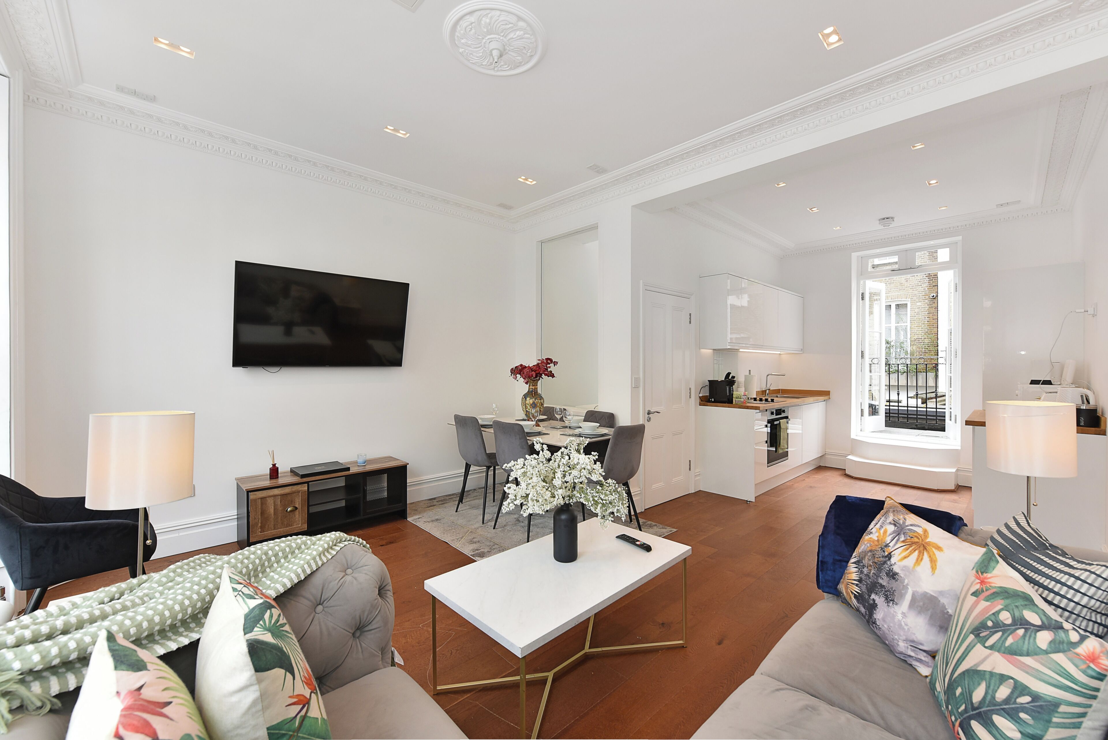 A spacious living area with a flat-screen TV, a dining table, and a kitchen in the background.