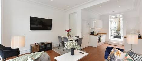 A spacious living area with a flat-screen TV, a dining table, and a kitchen in the background.