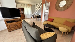 Un salon avec un canapé, un téléviseur, une table basse et, au fond, un coin repas.