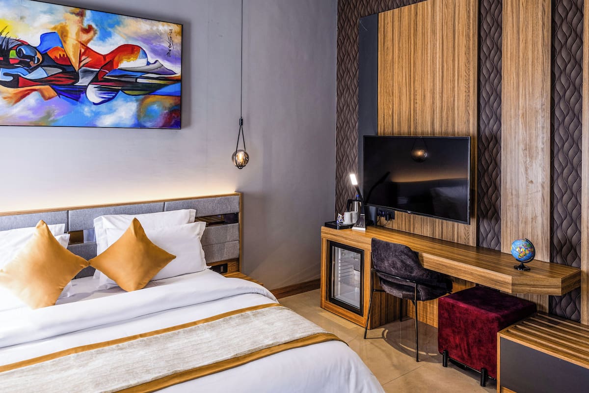 A hotel room with a bed, a desk with a computer, a TV, and a painting on the wall.