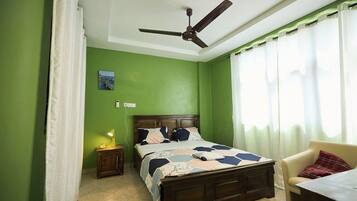 A bedroom with a bed, a nightstand, a table, a chair, a ceiling fan, and a window with curtains.