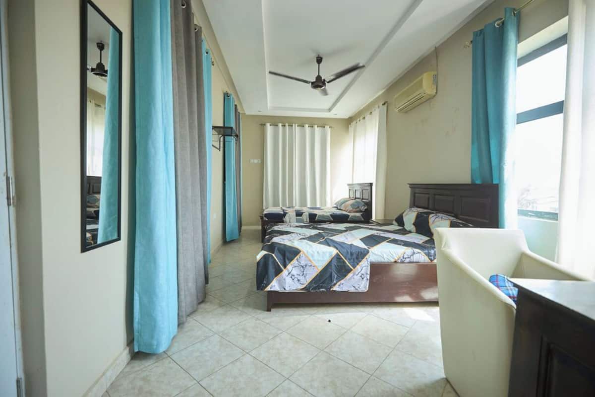 Un dormitorio con cama, escritorio, silla, ventilador de techo y ventana con cortinas.