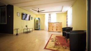 A spacious living room with a flat-screen TV, a wooden cabinet, and black chairs. - amp lodge (Kumasi)