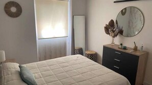 Een slaapkamer met een bed, een dressoir, een spiegel en een raam.