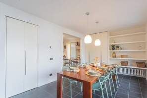 Un comedor moderno con una mesa de madera dispuesta para cuatro personas, rodeada de sillas color turquesa. Se ve un armario blanco y una estantería con adornos en el fondo.