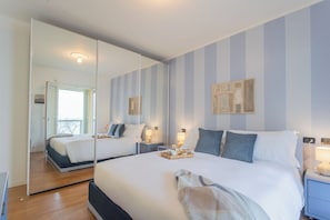 A hotel room with a large bed, a bedside table with a lamp, a mirror, and a view of the outside.