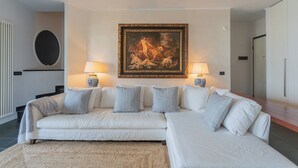 Ein modernes Wohnzimmer mit einem weißen Ecksofa, zwei Beistelltischen mit Lampen und einem großen gerahmten Gemälde an der Wand.