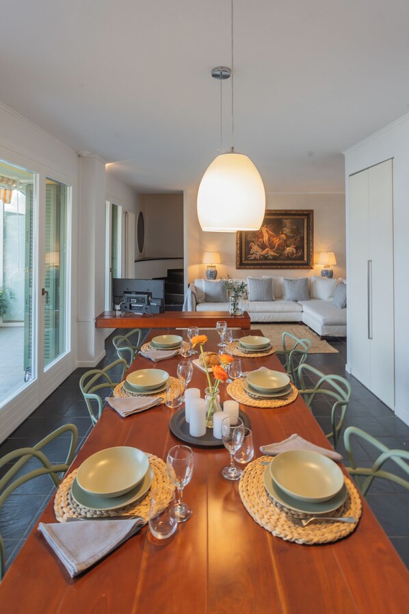 A dining area with a long wooden table set for six, surrounded by chairs. A large pendant light hangs above the table.