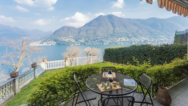 Eine Terrasse mit einem für Tee gedeckten Tisch, mit Blick auf einen See und Berge.