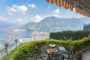 A terrace with a table set for tea, overlooking a lake and mountains.