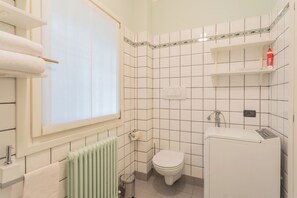 Un baño con un inodoro, un radiador, una ventana y un estante con artículos de tocador.