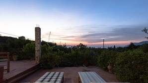 A patio with two sun loungers and a stone pillar, surrounded by greenery and a sunset view.
