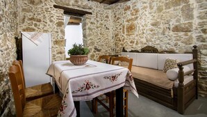 A rustic stone-walled room with a wooden table, chairs, a sofa, and a bed.