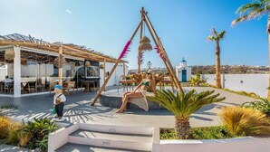 A rooftop terrace with outdoor seating, a swing, and a view of a church. - Amethyst Luxury Suites - Oia Junior Suite (Santorini)