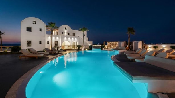 A swimming pool with lounge chairs, a white building with arched windows, and palm trees.